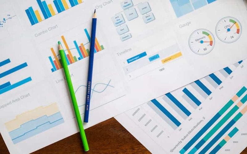 Flat lay of various business charts and colored pencils on wooden table, highlighting financial analysis.