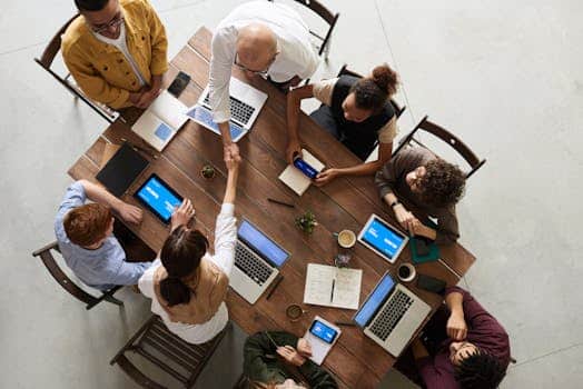 Top view of a diverse team collaborating in an office setting with laptops and tablets, promoting cooperation and strategic alignment